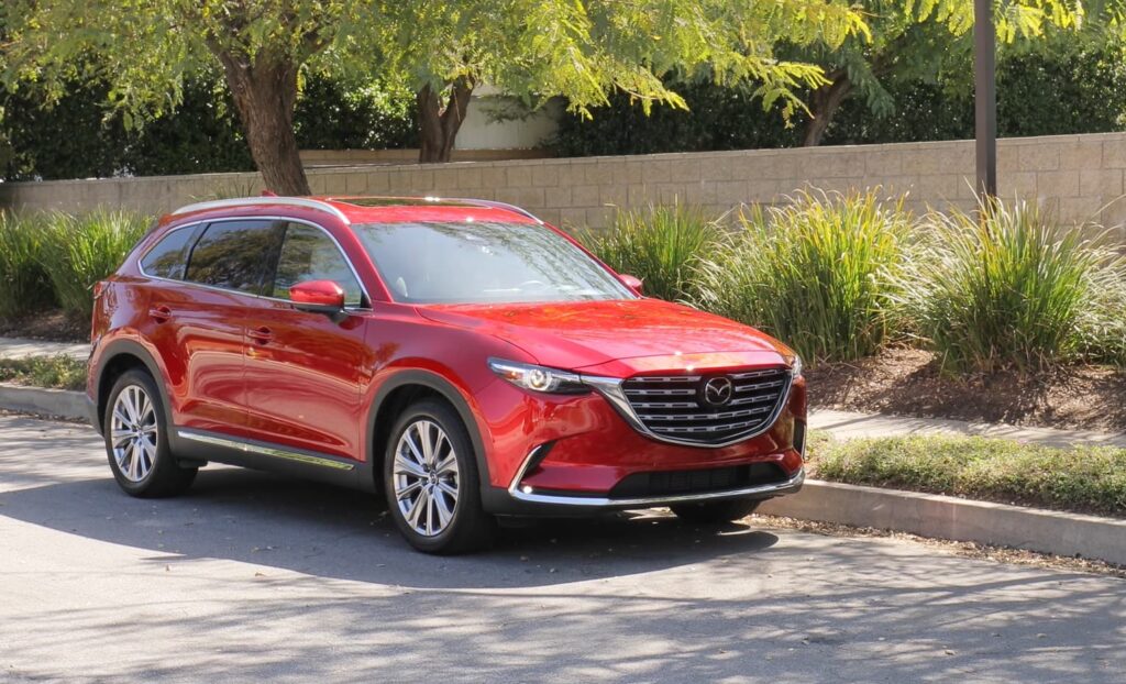 A red Mazda CX-9 parked on the side of the road with greenery in the background